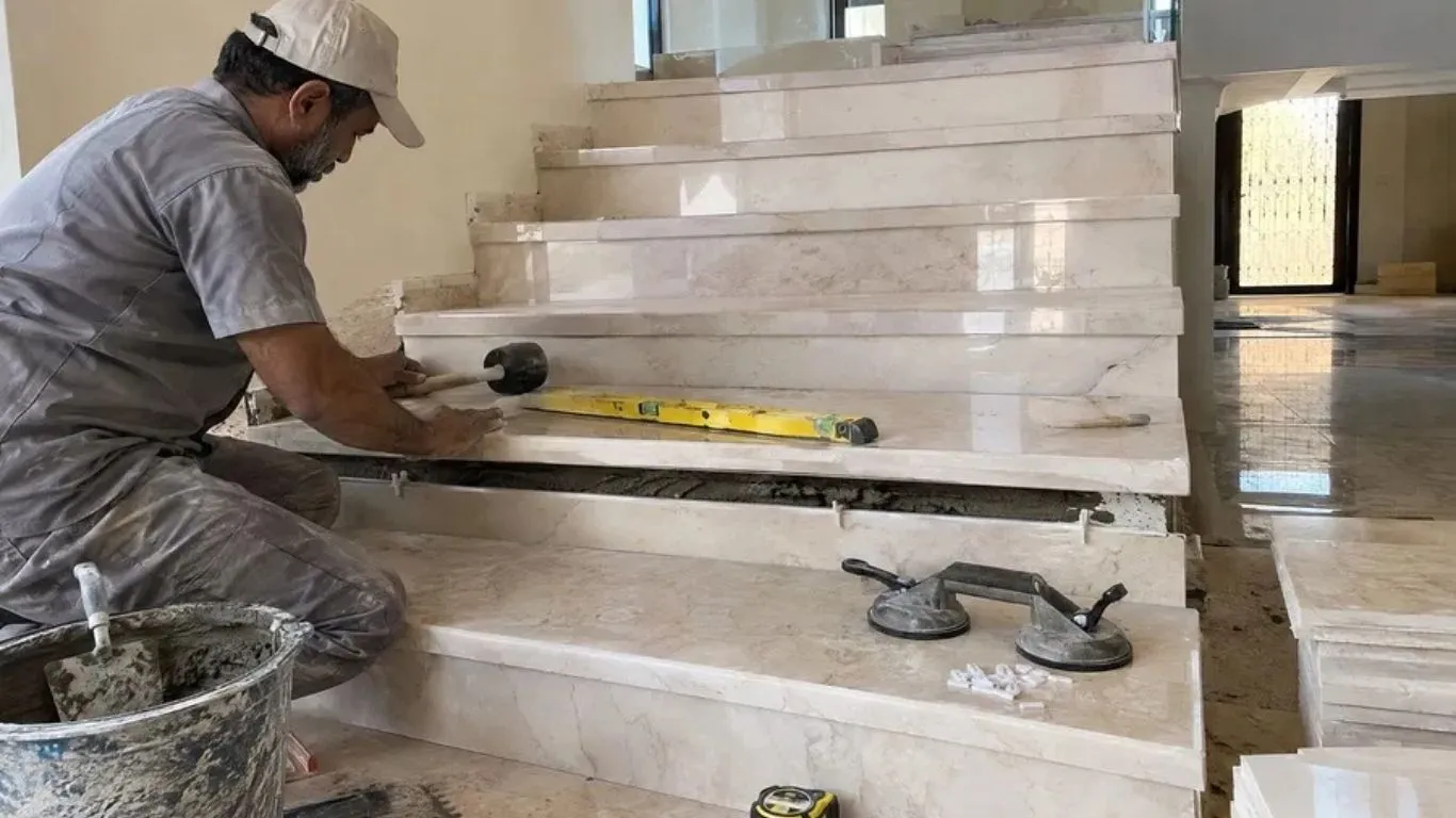 فني يضبط استواء درجة سلم رخامية باستخدام ميزان مياه